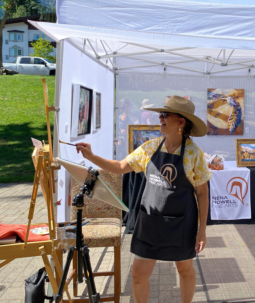 Nena Howell demos on a hot day with a large hat, easel at her art booth.